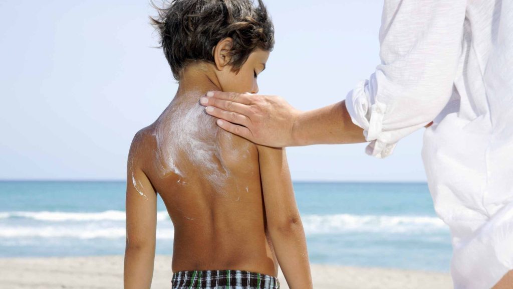 mujer poniendo crema solar a un niño enfrente del mar