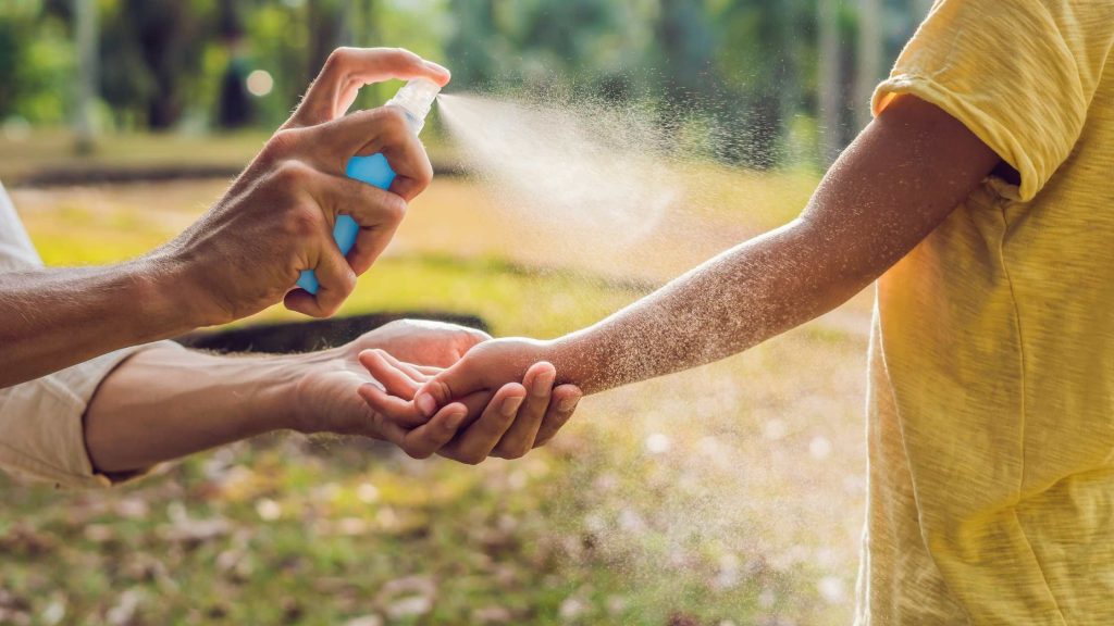 una persona adulta posant antimosquits en spray al braç d'un infant
